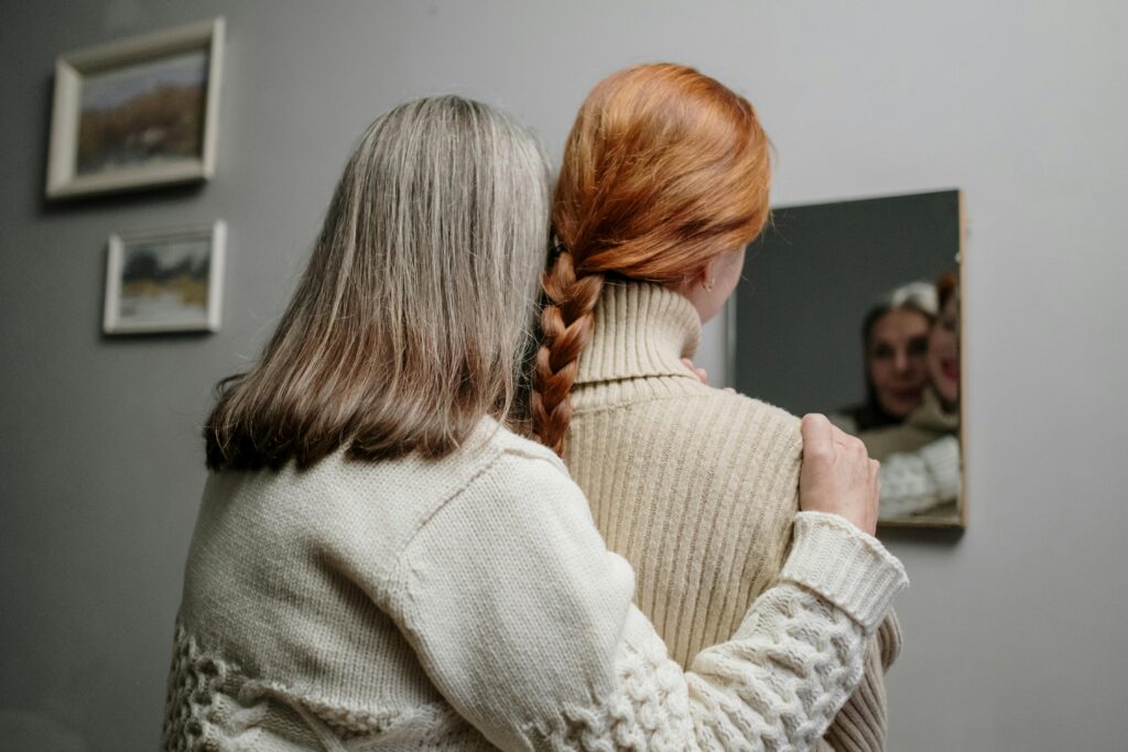 A touching moment of a mother and daughter in knitted sweaters reflected in a mirror.